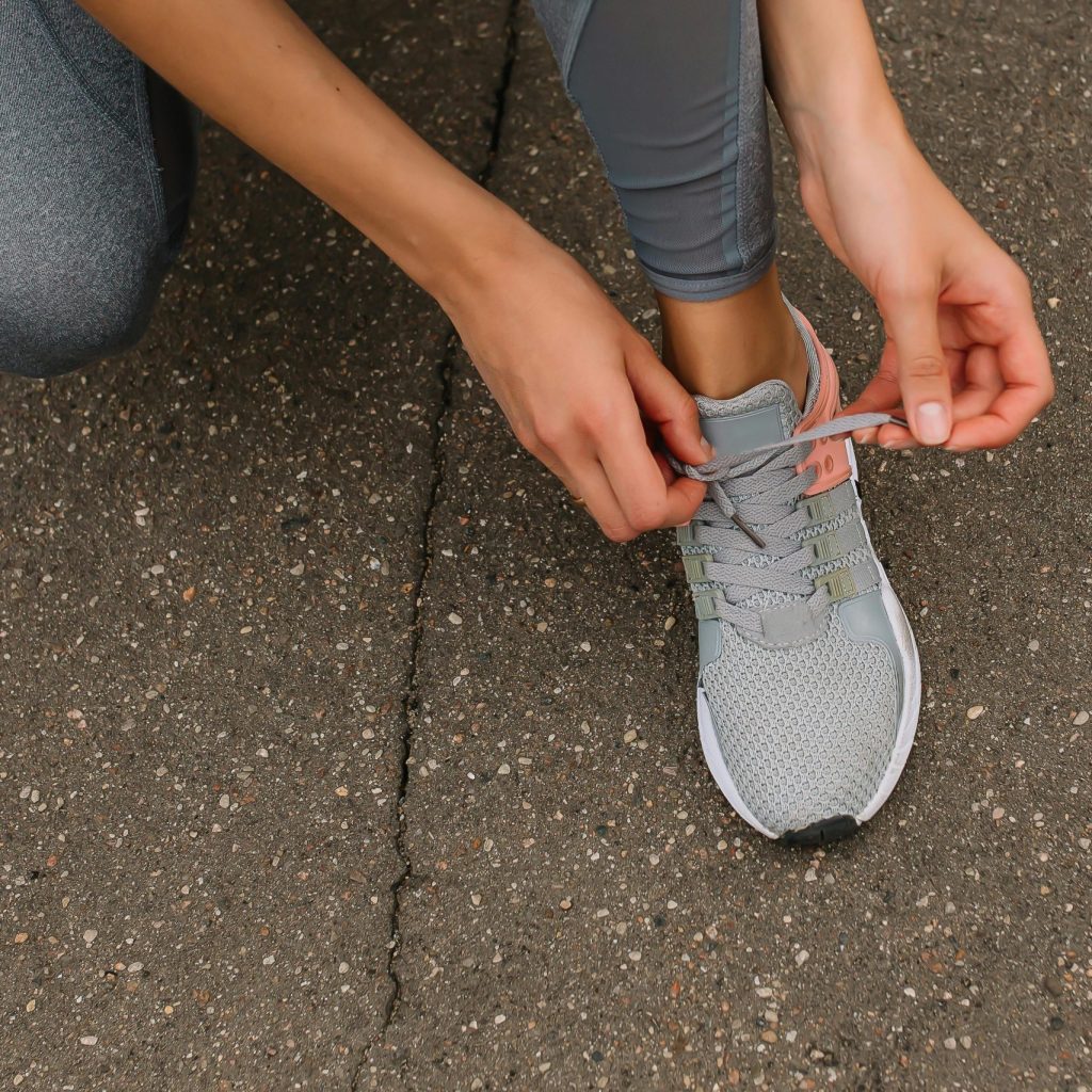 Close-up image of a person tying shoelaces on a sneaker while sitting on pavement.