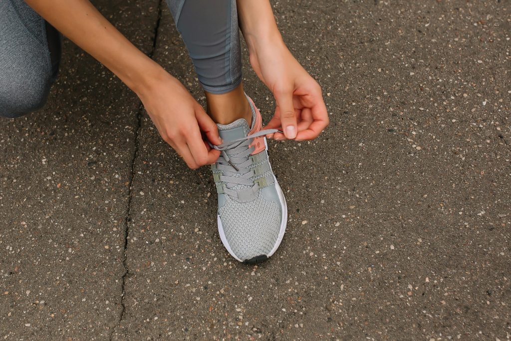 pexels-photo-8497536-8497536 Close-up image of a person tying shoelaces on a sneaker while sitting on pavement.
